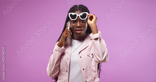 Pretty African American woman doing selfie shot on mobile phone isolated over pink background. © VAKSMANV