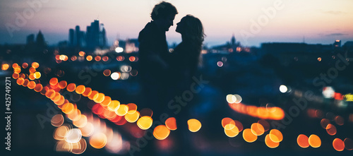 couple in rock-n-roll style standing on the roof in evening time at blured city lights background