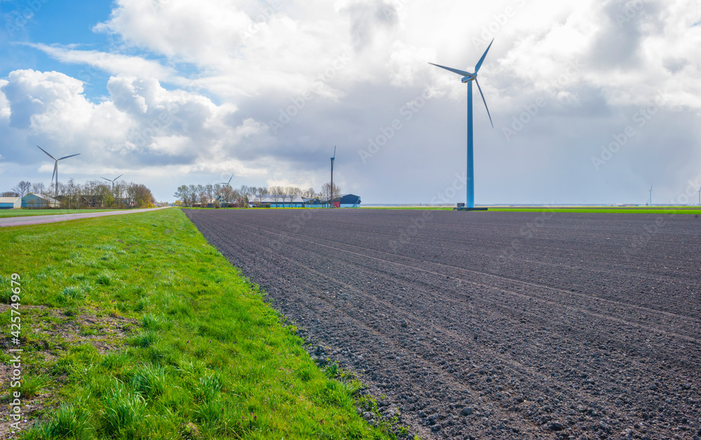 Furrows in a plowed field along a road in the countryside below a blue cloudy sky in spring, Almere, Flevoland, The Netherlands, April 5, 2021
