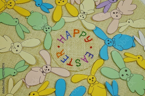 Multicolored Easter bunnies from colored paper on a white burlap, background