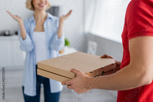 cropped view of happy woman showing wow gesture near delivery man with pizza boxes, blurred background