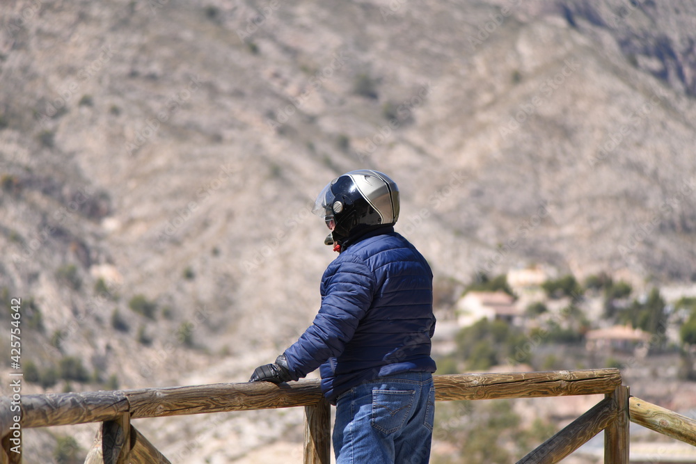 An elder man with a helmet stands at a wooden railing and looks to a scenic landscape in Spain. An elder man with a helmet stands at a wooden railing and looks to a scenic landscape in Spain.