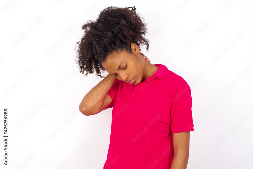 Obraz premium young beautiful African American woman wearing pink t-shirt against white wall suffering from back and neck ache injury, touching neck with hand, muscular pain.