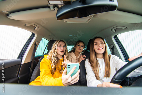Three happy girlfriends go on a trip. Three women ride in the car, look at the phone to fing corect direction.