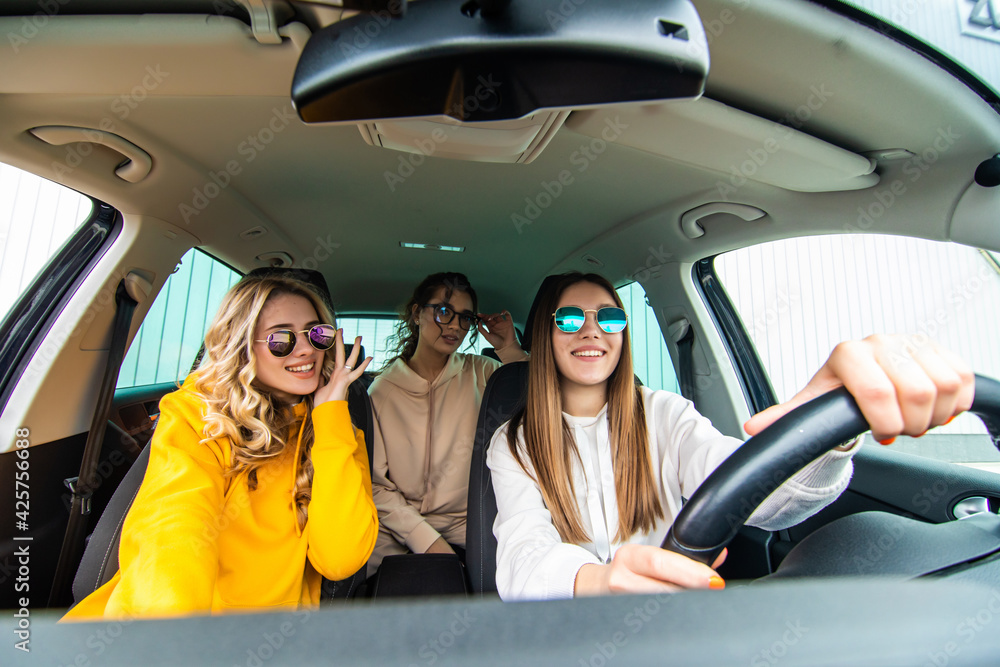 Three female friends in sunglasses enjoying traveling in the car.