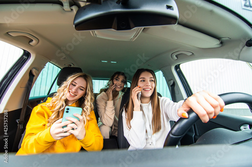 Three best friends women in the car and uses smart phones while drive car in road trip