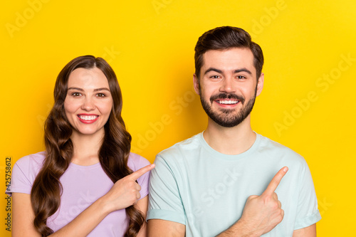 Portrait of attractive cheerful couple girl showing copy empty blank space isolated over bright yellow color background