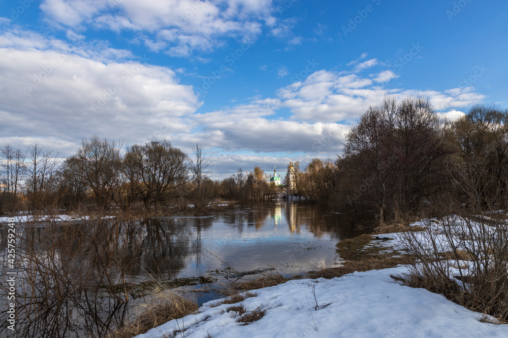 Spring flood. High water. Church on the banks of the river. Rural landscape in early spring. Clouds and trees reflected in the water. Spring flood. High water. Church on the banks of the river. Rural landscape in early spring. Clouds and trees reflected in the water.