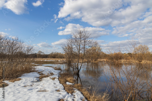 Spring flood, the river overflowed its banks. High water level in the river. Rural landscape in early spring. Clouds and trees are reflected in the water.