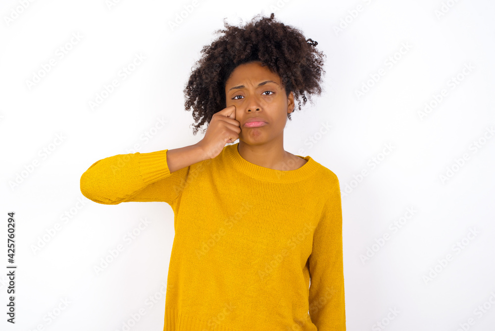 Disappointed dejected young beautiful African American woman wearing yellow sweater against white wall wipes tears stands stressed with gloomy expression. Negative emotion Disappointed dejected young beautiful African American woman wearing yellow sweater against white wall wipes tears stands stressed with gloomy expression. Negative emotion