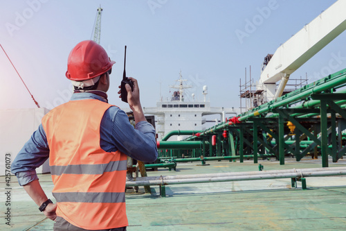Workers Wearing a reflective vest and hand holding walkie talkie, communication radio on deck oil tanker ship during ship repair and maintenance in shipyard pipe system background