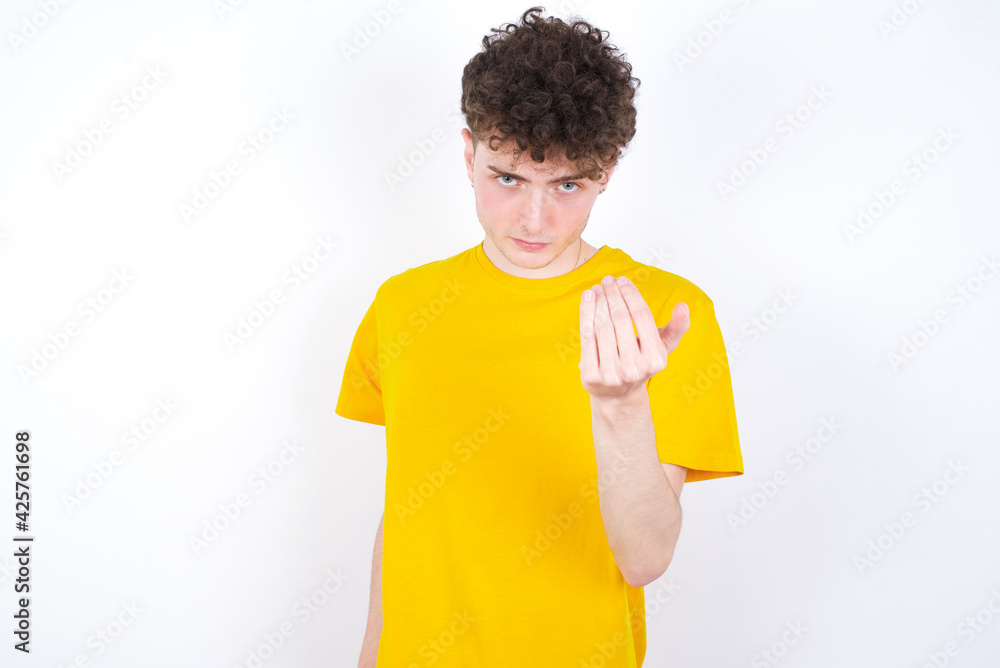 young caucasian handsome man with curly hair wearing yellow T-shirt against white studio background  inviting to come with hand. Happy that you came