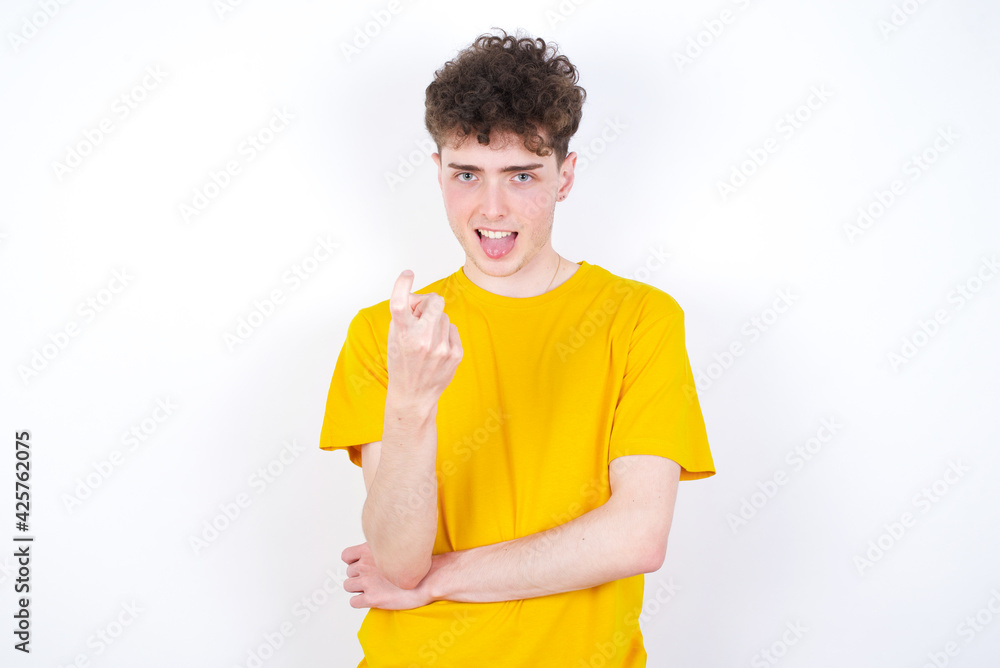 young caucasian handsome man with curly hair wearing yellow T-shirt against white studio background Beckoning come here gesture with hand inviting welcoming happy and smiling young caucasian handsome man with curly hair wearing yellow T-shirt against white studio background Beckoning come here gesture with hand inviting welcoming happy and smiling