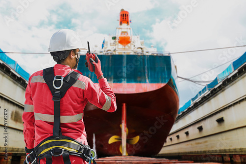 Workers wearing full safety harness and hand holding communication radio at floating dry dock in shipyard for safety concept