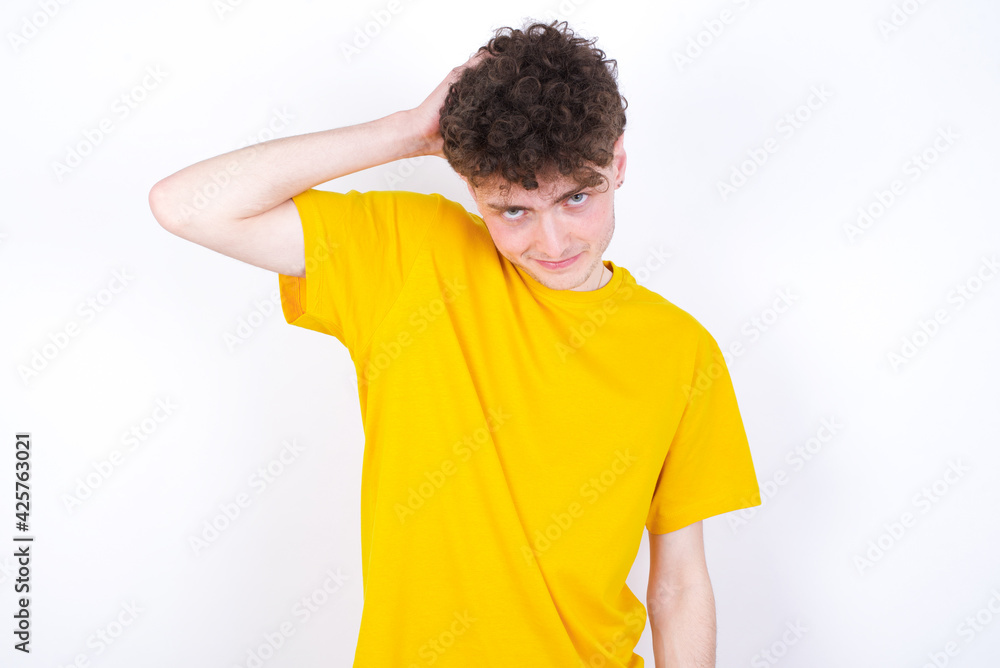 young caucasian handsome man with curly hair wearing yellow T-shirt against white studio backgrobeing confused and wonders about something. Holding hand on head, uncertain with doubt. Pensive concept. young caucasian handsome man with curly hair wearing yellow T-shirt against white studio backgrobeing confused and wonders about something. Holding hand on head, uncertain with doubt. Pensive concept.