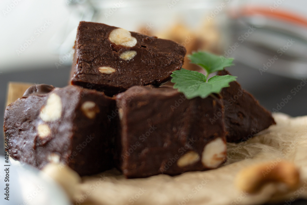 Homemade chocolate fudge garnished with mint leaves and served with tea on a black background. Nuts in the background blurred background. Copy space. Homemade chocolate fudge garnished with mint leaves and served with tea on a black background. Nuts in the background blurred background. Copy space.