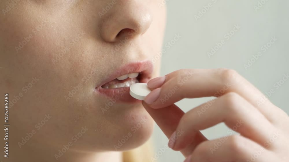 close up of a woman taking a white pill and drinking water. close up of a woman taking a white pill and drinking water.