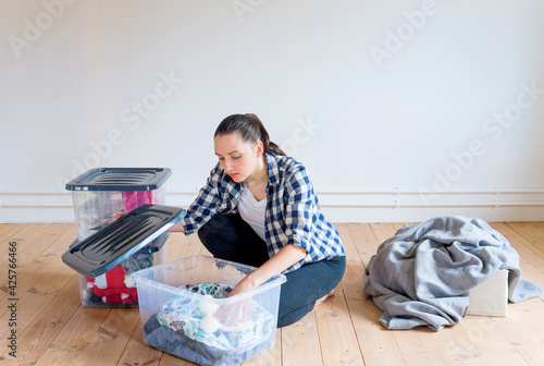 A young woman puts away seasonal clothes and items for storage in boxes. Spring cleaning.