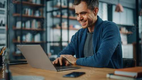 Handsome Caucasian Man Working on Laptop Computer while Sitting Behind Desk in Cozy Living Room. Freelancer Working From Home. Browsing Internet, Using Social Networks, Having Fun in Flat.