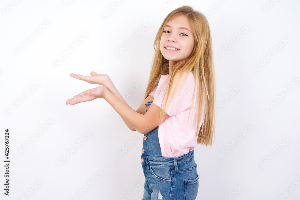 beautiful caucasian little girl wearing denim jeans overall over white background pointing aside with hands open palms showing copy space, presenting advertisement smiling excited happy beautiful caucasian little girl wearing denim jeans overall over white background pointing aside with hands open palms showing copy space, presenting advertisement smiling excited happy