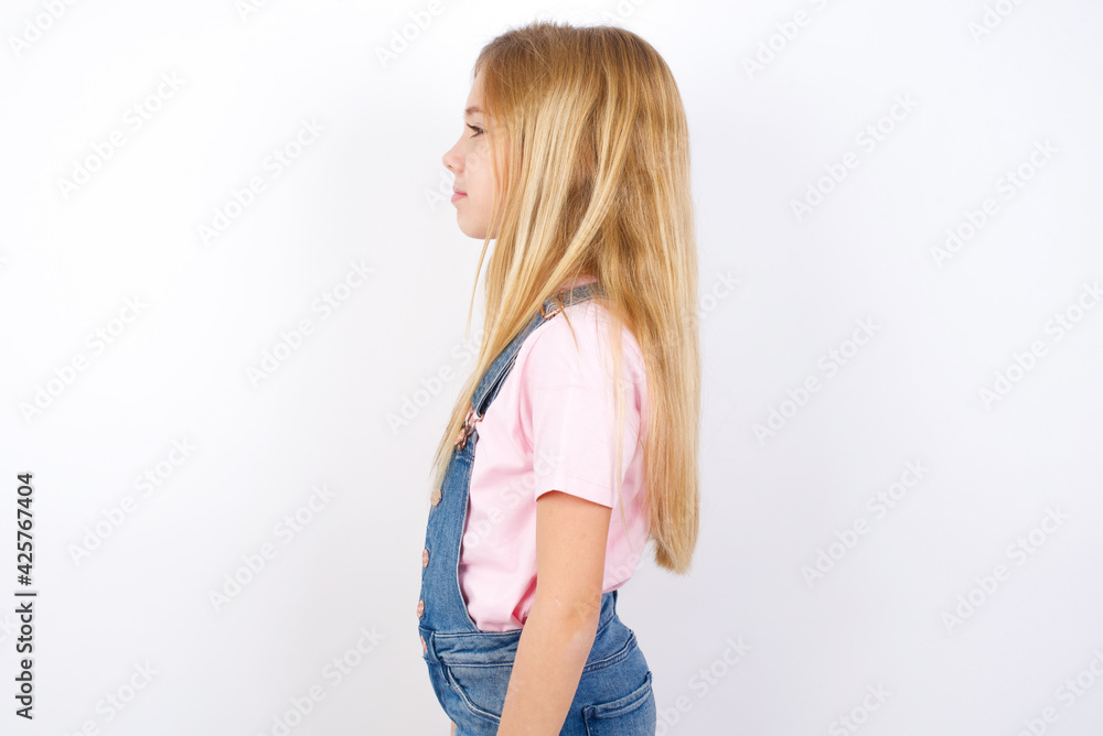Fotka „beautiful caucasian little girl wearing denim jeans overall over  white background looking to side, relax profile pose with natural face with  confident smile.“ ze služby Stock | Adobe Stock