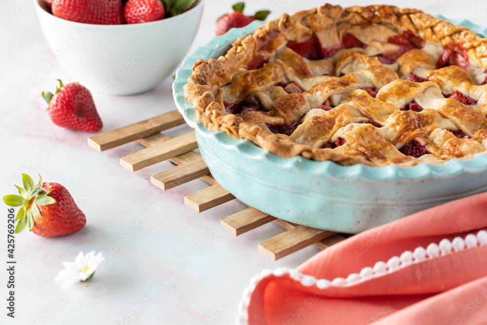 Close up of a homemade lattice topped strawberry and rhubarb pie cooling on a wooden trivet. Close up of a homemade lattice topped strawberry and rhubarb pie cooling on a wooden trivet.
