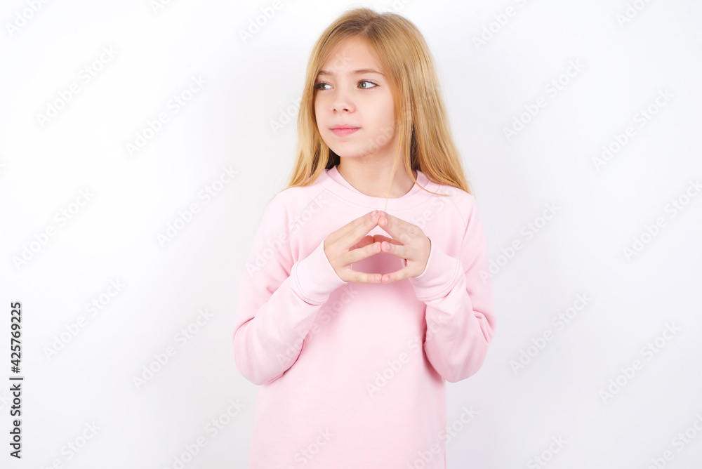 Beautiful caucasian blonde little girl wearing pink sweater steepls fingers and looks mysterious aside has great evil plan in mind Beautiful caucasian blonde little girl wearing pink sweater steepls fingers and looks mysterious aside has great evil plan in mind