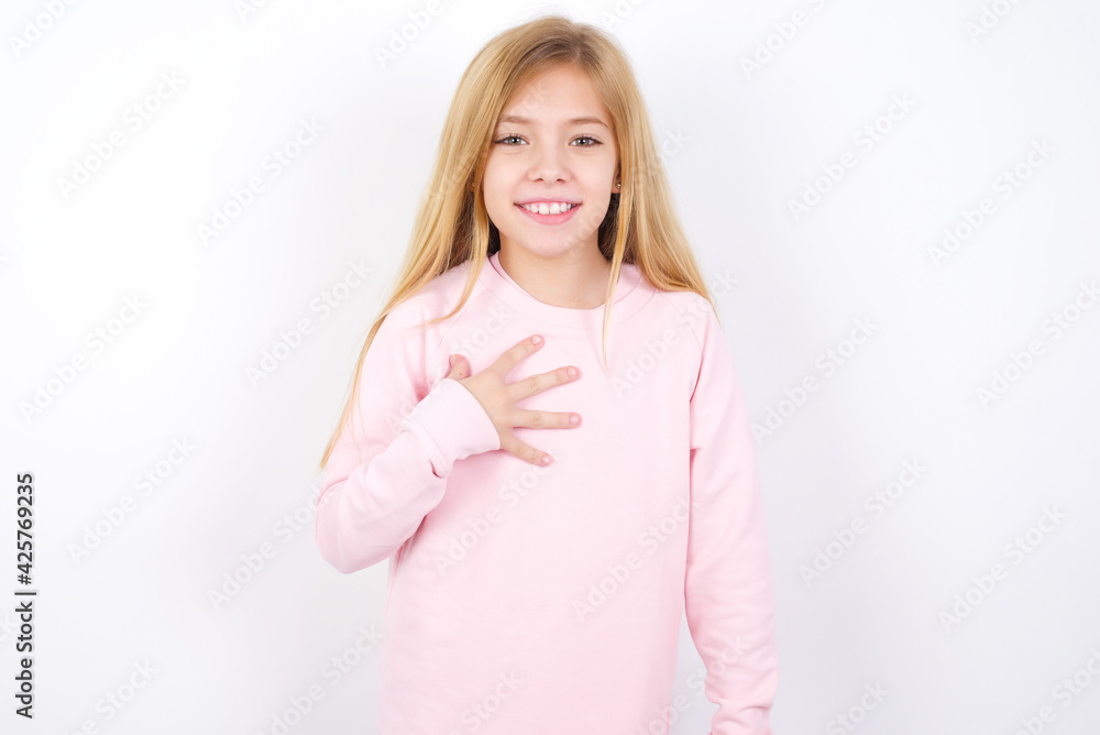 Beautiful caucasian blonde little girl wearing pink sweater smiles toothily cannot believe eyes expresses good emotions and surprisement