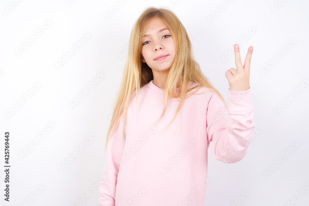Beautiful caucasian blonde little girl wearing pink sweater smiling and looking friendly, showing number two or second with hand forward, counting down Beautiful caucasian blonde little girl wearing pink sweater smiling and looking friendly, showing number two or second with hand forward, counting down