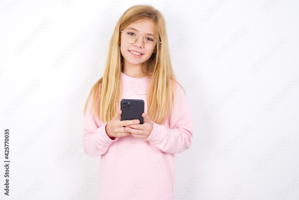 beautiful caucasian little girl wearing pink sweater Mock up copy space. Using mobile phone, typing sms message beautiful caucasian little girl wearing pink sweater Mock up copy space. Using mobile phone, typing sms message