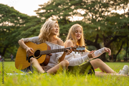 Portrait of caucasian young women sitting in the park outdoor and playing a guitar sing a song together with happiness © ronnachaipark