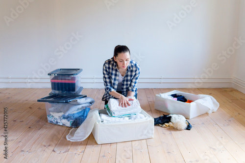 A young woman puts away seasonal clothes and items for storage in boxes. Spring cleaning