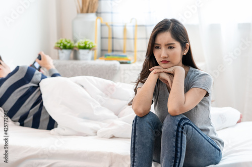 Fotografie Asian young upset woman sitting on the bed, against her boyfriend, Wife has an expression of disappointment and upset with her husband