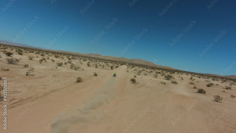 Four-wheeler driving along a dusty trail in the Mojave Desert on a hot day - aerial first person view Four-wheeler driving along a dusty trail in the Mojave Desert on a hot day - aerial first person view