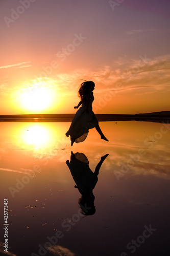 girl in a long dress on a salty pink lake against the background of a bright sunset. dark silhouette in flight