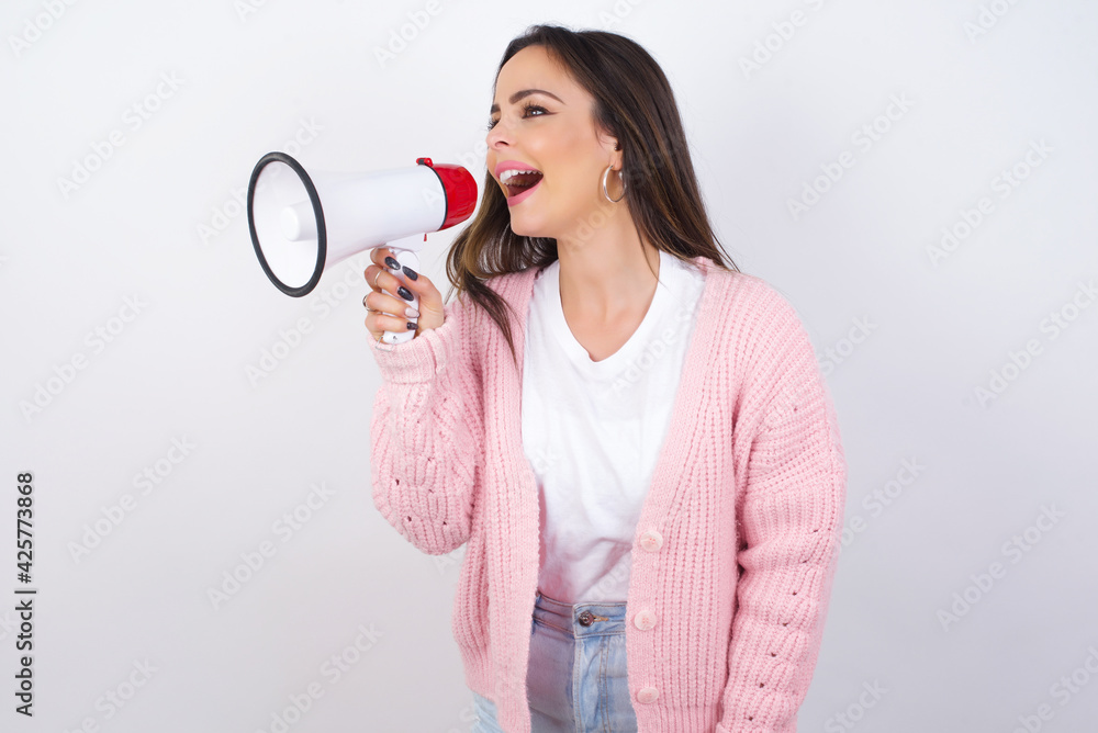 young beautiful caucasian woman wearing pink knitted jacket over white wall Through Megaphone with Available Copy Space young beautiful caucasian woman wearing pink knitted jacket over white wall Through Megaphone with Available Copy Space