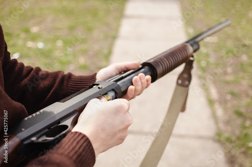 A man charges a pump-action shotgun with a Ammo. 12 caliber. Tyre outdoor. A man in headphones and goggles is preparing to shoot. Firearms for sports shooting, hobby. copy space