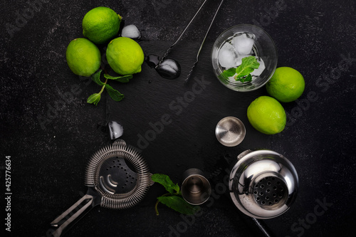 Bar tools. Ingredients for mojito cocktail with lime, mint leaves, ice. Cold drink and beverages preparation. Black table, top view with copy space