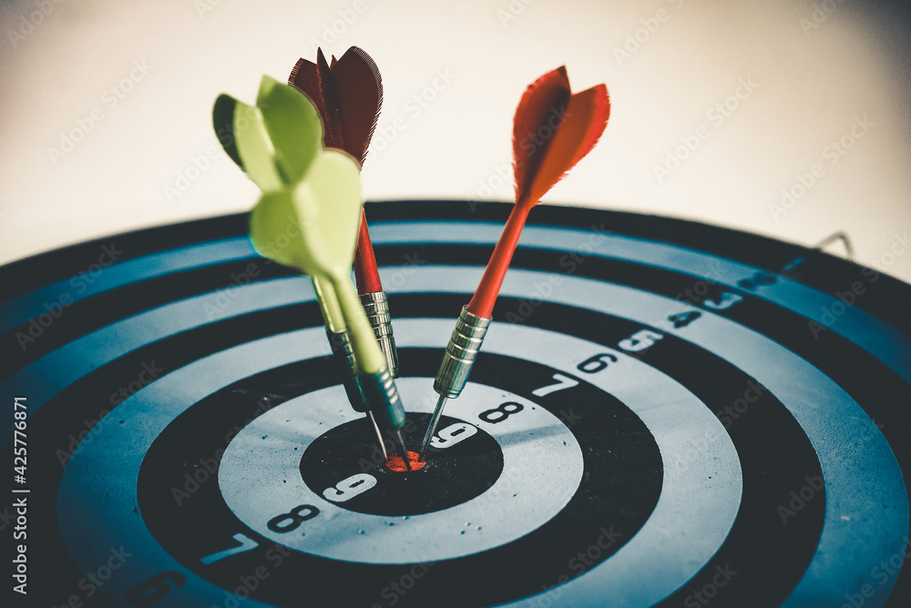 Close up shot of the dart arrow hit on bulleyes of dartboard to represent that the business reached the target of company with dark tone picture style. Target and goal as concept. Close up shot of the dart arrow hit on bulleyes of dartboard to represent that the business reached the target of company with dark tone picture style. Target and goal as concept.
