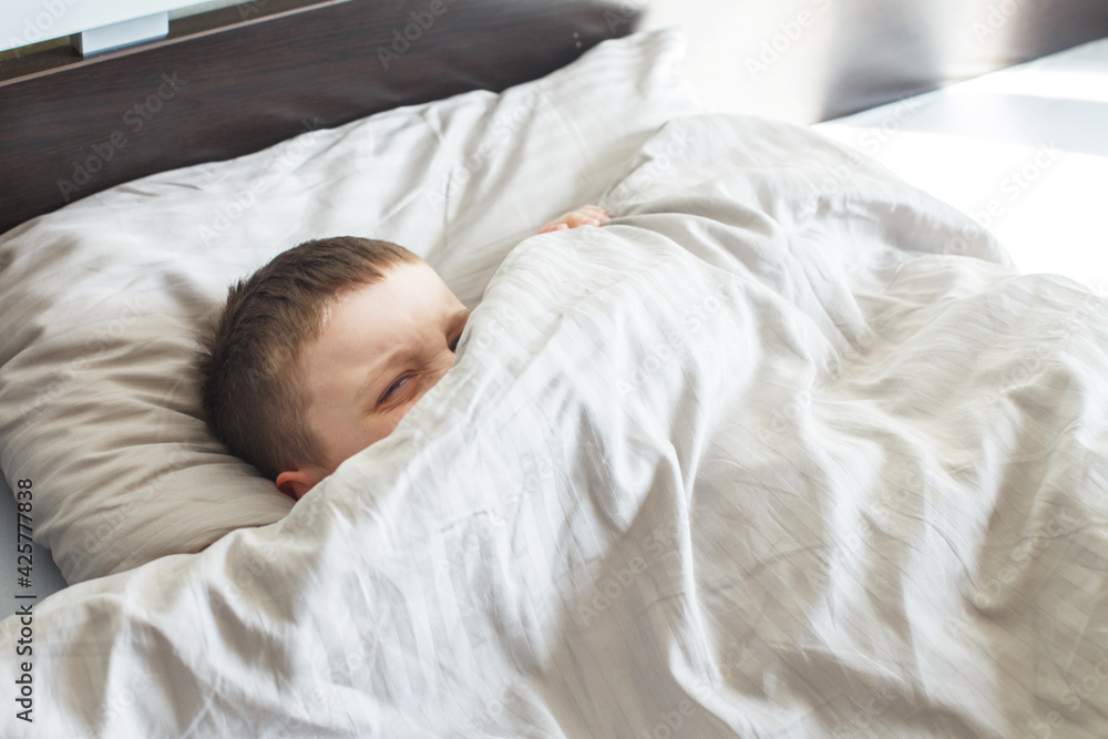 boy sleep in the bed. child lies on pillow and covers his face with a blanket boy sleep in the bed. child lies on pillow and covers his face with a blanket