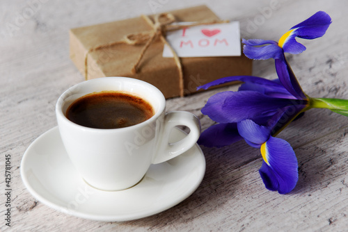 Obraz na płótnie White cup of coffee, gift box with message for mom and iris flower on gray wood table. Mother's Day holiday concept. w salonie