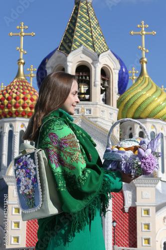 Russian woman with colorful Easter eggs, Easter cake in basket. Easter in Orthodox Saint Igor Chernigovsky's church in Novo-Peredelkino, Moscow city, Russia. Holiday decor, Easter decoration. Landmark photo