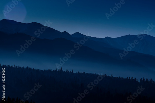 Tatra Mountains and the hills at night. The valleys are hidden in the fog, silhuettes of the trees can be seen from the shadows. Selective focus on the ridge, blurred background.
