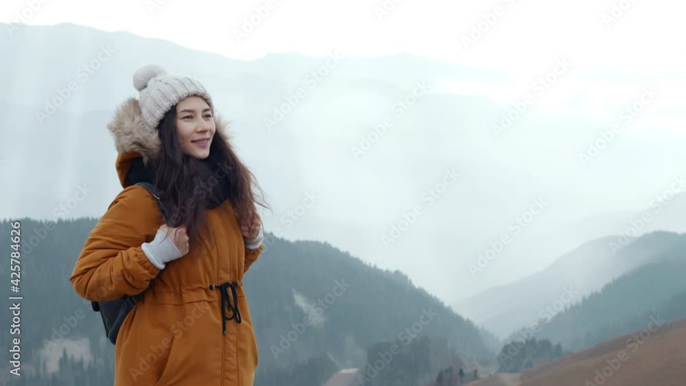 Happy asian woman tourist enjoys breathing fresh air high in cloudy mountains at cold weather. Young hiker at amazing hazy background of mountain landscape in smoke. Concept of active lifestyle Happy asian woman tourist enjoys breathing fresh air high in cloudy mountains at cold weather. Young hiker at amazing hazy background of mountain landscape in smoke. Concept of active lifestyle