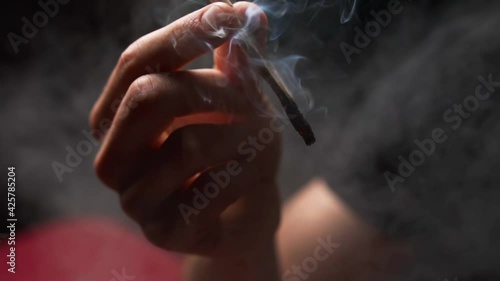 The man is addicted to weed drugs and smokes a twisted joint of cannabis. Smoke comes from a cigarette. Unconventional marijuana treatment.