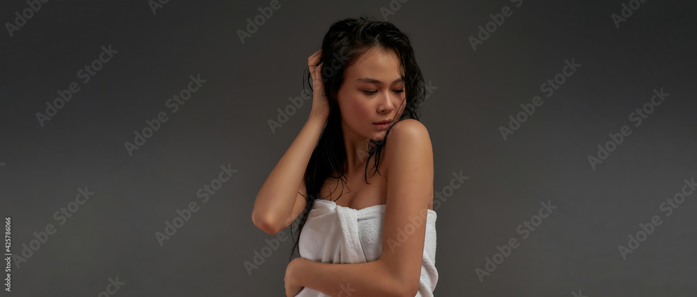 Young beautiful asian half naked woman with with eyes closed and touching her hair in bath towel 