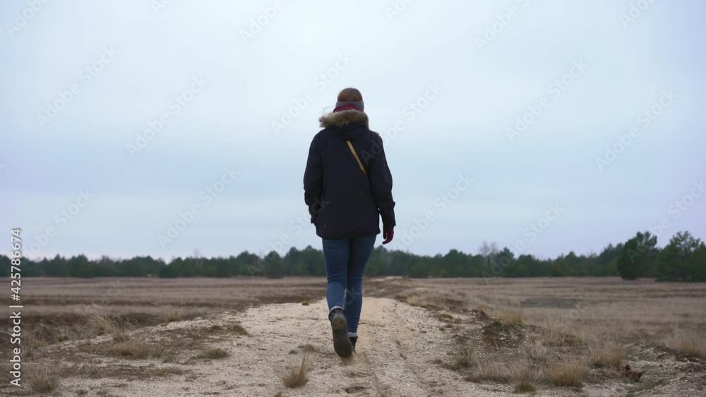 Female hiker walking away from camera in countryside field, rear view Female hiker walking away from camera in countryside field, rear view