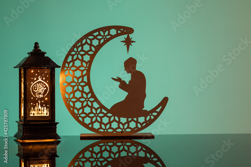 Eid Mubarak concepts with lamp inscribed with arabic text translated to english as Ramadhan is our light., with crescent moon in silhouette