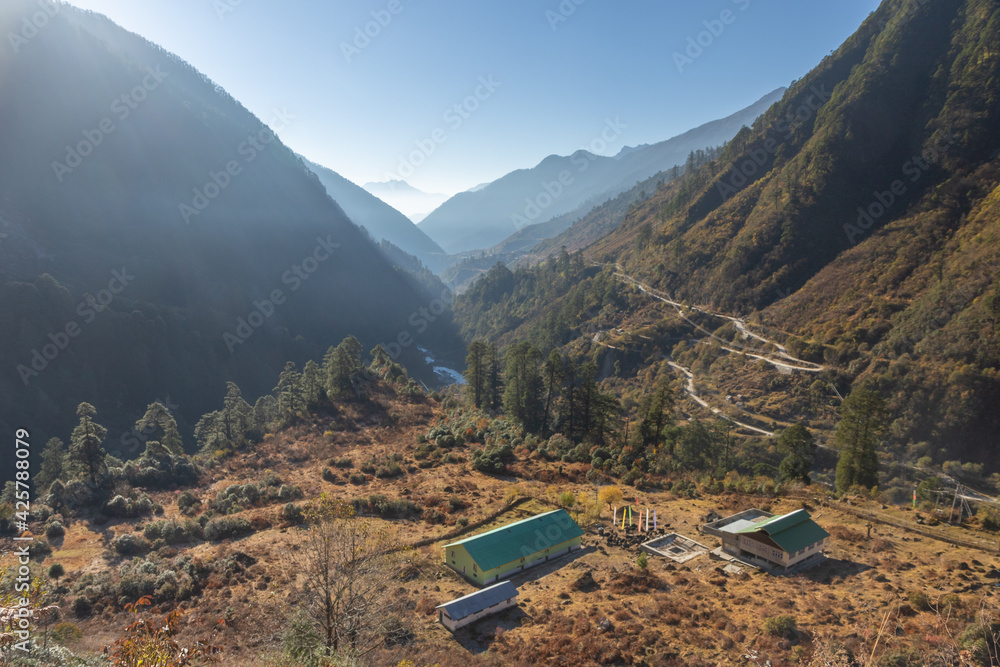 View of a few houses and Tibetan prayer flags in a Valley surrounded by mountains and a road going down in Sikkim India on 22 November 2016