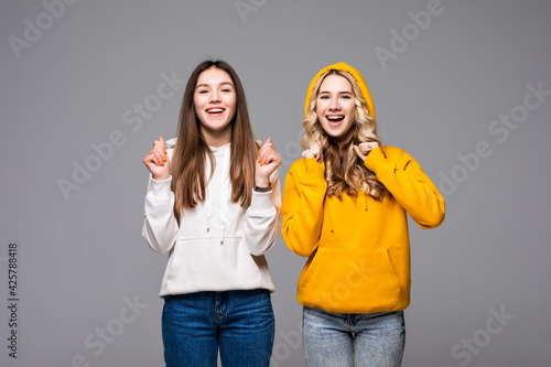 Two young women doing winner gesture celebrating isolated on gray background
